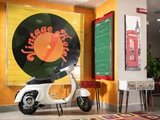 En hvid vintagescooter er parkeret indendørs ved siden af et stort Vintage Hotel-skilt, en fodboldtaktiktavle, et rødt telefonboksfoto og et lille skuffe-bord.