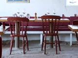 To tomme træstole ved et bord med vinglas og vandglas, inde i en restaurant med sand på gulvet og rødbrune stole.