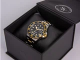 Et armbåndsur i sort og guld med en sort urskive ligger i en åben sort æske med mærket Schmidt Watches på indersiden af låget.