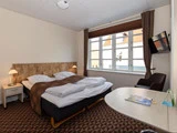 Et pænt hotelværelse med en dobbeltseng, brune tæpper, natborde med lamper, et stort vindue, et væghængt tv, en stol og et skrivebord.