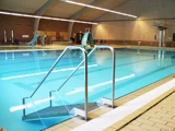 Indendørs swimmingpool med klart blåt vand, metalgelændere ved indgangen, rutsjebaner, springbrætter og murstensvægge i baggrunden.