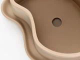 En beige, uregelmæssigt formet vask med glatte, buede kanter og et centralt afløbshul på en hvid baggrund.