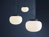 Tre runde, hvide pendler med sorte ledninger hænger op ad en mørkeblå væg og skaber et moderne og minimalistisk look.