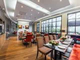 Moderne restaurantinteriør med pænt dækkede borde, stribede og røde stole, store vinduer, trægulv og dekorative blomsterarrangementer.