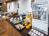 Hotellets morgenmadsbuffet med forskelligt bagværk, frugt, juice, bestik og en kølemontre med yoghurt og skåle, alt sammen pænt arrangeret på en trædisk.