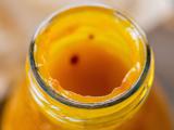 Nærbillede af mundingen på en glasflaske fyldt med tyk, gul-orange væske, muligvis juice eller sauce, med rester rundt om kanten.