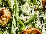 Nærbillede af en cæsarsalat med romainesalat, strimlet parmesanost, croutoner og cremet dressing.