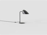 En moderne sort bordlampe med en buet lampeskærm og et slankt stativ står på en hvid overflade, mens ledningen og afbryderen hænger bagved.