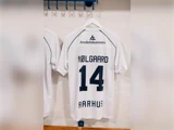 Hvid fodboldtrøje med NØLGAARD og 14 på ryggen samt Andelskassen-logoet og AARHUS trykt på, hængende på et vægstativ.