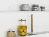 En køkkenhylde med stablede grå skåle, stribede kopper, en krukke med konserverede citroner, en morter og støder i træ og en køkkenrulleholder med træstang og marmorsokkel.