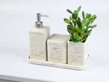 Et badeværelsessæt i marmor med en sæbedispenser, en beholder med låg og en grøn plante i en matchende holder, alt sammen placeret på en rektangulær bakke.