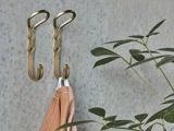 To messingkroge på en grå, plettet væg, hvoraf den ene bærer et beige klæde. En grøn bladplante til højre i billedet.