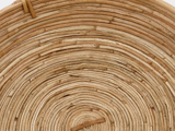 Nærbillede af en vævet kurv lavet af naturlige, lysebrune fibre arrangeret i et cirkulært spiralmønster.
