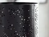 Nærbillede af en sort metalcylinder med mange uregelmæssigt formede huller, der skaber et dekorativt perforeret mønster.