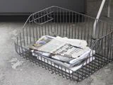 En trådkurv på et betongulv indeholder foldede aviser og magasiner.