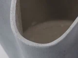 Nærbillede af kanten og det indre af en grå, glat, cylindrisk vase af keramik eller beton med en buet, uregelmæssig åbning.