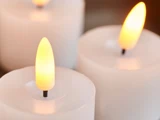 Tre hvide stearinlys med glødende flammer står tæt samlet og skaber en blid, varm og beroligende stemning.