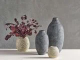 Tre strukturerede grå vaser og en cremefarvet vase med prikket mønster på et bord; den cremefarvede vase indeholder mørkerøde eukalyptusgrene.