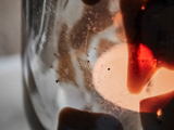 Nærbillede af en glaskrukke med kafferester og -striber, belyst af varmt lys bagfra, hvilket skaber en blød, abstrakt effekt.