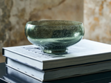 En gennemsigtig grøn glasskål står oven på to stablede indbundne bøger med hvide omslag på en mørk bordplade.