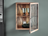 Et lille væghængt træskab med glasdør, der indeholder to grønne glas på den øverste hylde og grønne skåle og tallerkener på den nederste hylde.
