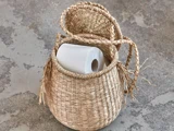 En rulle toiletpapir i en rund, flettet kurv med låg, der står på en grå betonoverflade.