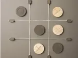 Tic-tac-toe-spil på en væg med et gitter lavet af reb; store X- og O-brikker af træ placeret på brættet.