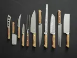 Et sæt med elleve køkkenknive og -redskaber med træhåndtag arrangeret i en række på en mørk overflade.
