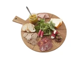 Rundt serveringsbræt i træ med forskellige oste, kødpålæg, kiks, brødskiver, radiser, oliven, rucola og et glas chutney med en ske.
