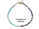 Et fint armbånd med lyseblå og lilla ædelstensperler, adskilt af små guldperler, vist på en hvid baggrund med dansk tekst Armbånd med ædelsten.