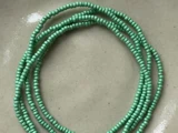Flere tråde af små, runde, mintgrønne perler er viklet på en lys beige overflade.
