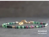 Et delikat ædelstensarmbånd med små grønne, rosa og guldfarvede perler på en grå overflade. Teksten lyder: Armbånd med ædelsten.