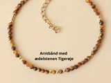 Et perlearmbånd med brune og gyldne tigerøje-ædelsten og en guldkædeforlænger, vist på en beige baggrund. Dansk tekst: Armbånd med ædelstenen Tigerøje.
