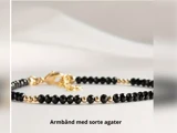 Et fint armbånd med skiftevis sorte agat- og guldperler på en lys baggrund. Teksten nedenunder lyder: Armbånd med sorte agater.