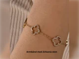 Guldarmbånd med zirkonia sten blomsterformede led på et håndled, teksten nedenunder lyder Armbånd med Zirkonia sten (Armbånd med zirkonia sten) på dansk.