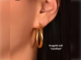 Et nærbillede af en kvindes øre med en snoet guldørering. Teksten på billedet lyder: Forgyldt stål vandfast.