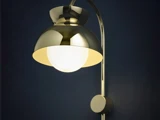 En moderne væglampe med en skinnende metalskærm og en lysende hvid pære, der fremstår mod en mørkeblå baggrund.