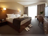 Moderne hotelværelse med en stor seng, to par tøfler, badekåber, fladskærms-tv, skrivebord med stole og store vinduer med gardiner, der lukker naturligt lys ind.