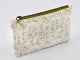 En cremefarvet stofpose med et blomstermønster i guld og en lynlås i guld, vist på en almindelig hvid baggrund.