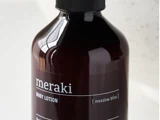 En mørk flaske mærket meraki BODY LOTION [meadow bliss] med sort hætte, vist mod en sløret lys baggrund.