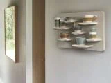 Et væghængt display med forskellige keramiske kopper og krus på buede hylder, placeret i et moderne, minimalistisk interiør.