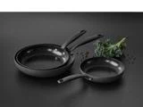 Tre sorte nonstick-pander i forskellige størrelser står på en mørk flade med grønkålsblade og peberkorn ved siden af.