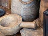 Nærbillede af rustikt køkkenudstyr i træ, bl.a. en rund skål med hank og et stort kar, placeret på en træoverflade.