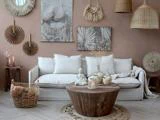 En hyggelig stue med en hvid sofa, et rundt sofabord i træ, flettede kurve, rattanindretning, stearinlys og vægkunst i jordfarver, der skaber en varm boho-atmosfære.