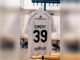 En hvid fodboldtrøje, der hænger i et omklædningsrum, med navnet Emmery, nummeret 39 og Aarhus på ryggen.