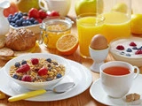 Et morgenbord med müsli med bær, et kogt æg, te, appelsinjuice, yoghurt med frugt, brød, marmelade og frisk frugt.