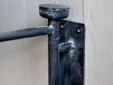 Nærbillede af et vægbeslag af metal med to skruer, der er fastgjort til en væg og støtter en vandret stang; metallet har svejsemærker.