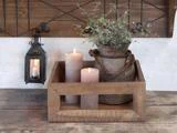 På en rustik træbakke står to tændte stearinlys og en potteplante på et træbord. En lille lanterne med et stearinlys hænger på væggen i nærheden.