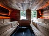 En moderne træsauna med bænke i flere niveauer, varm belysning og store vinduer, der viser en snedækket skov udenfor.