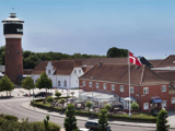 En rød murstensbygning med navnet Tønderhus med et dansk flag udenfor, et rundt vandtårn og træer under en klar blå himmel.